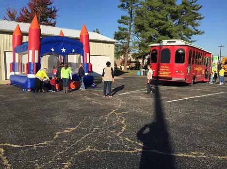 People standing near an inflatable bounce house and a red trolley bus