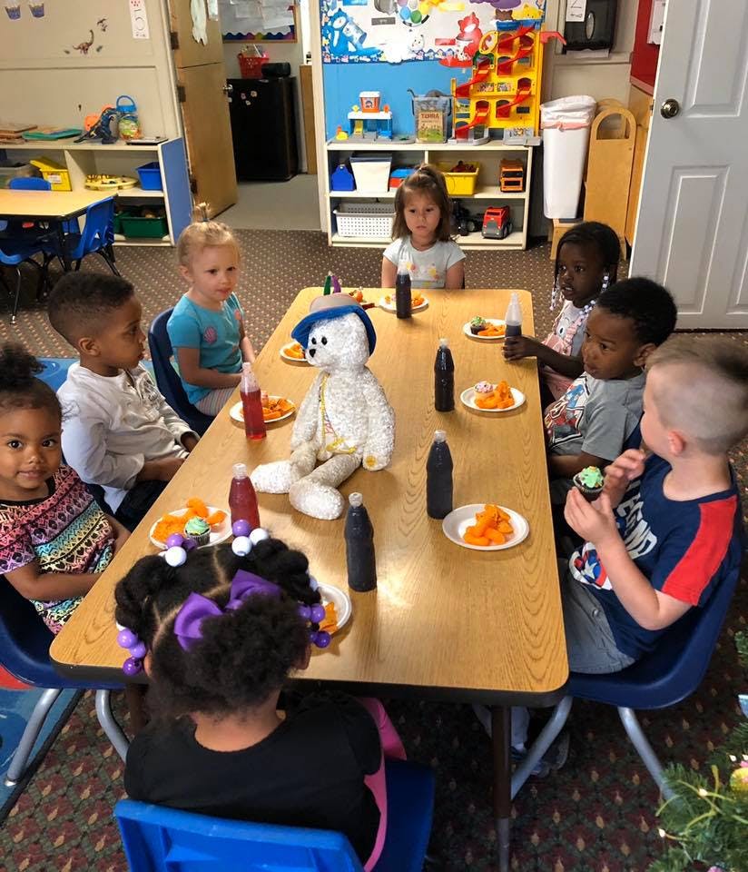 Children and a stuffed animal sitting around a table with snacks