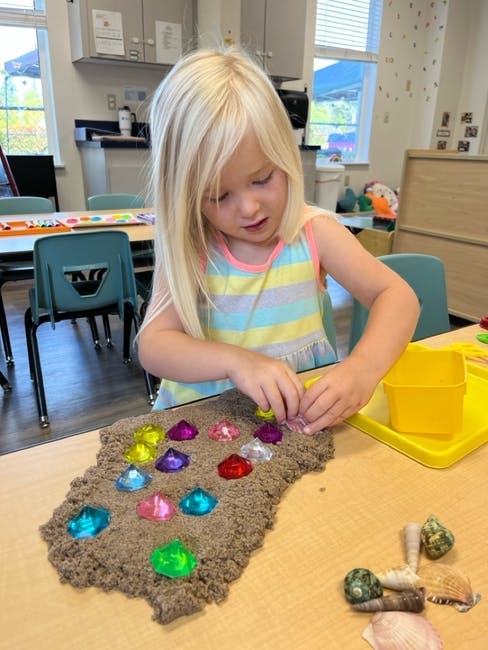 Child playing with kinetic sand and colorful gems