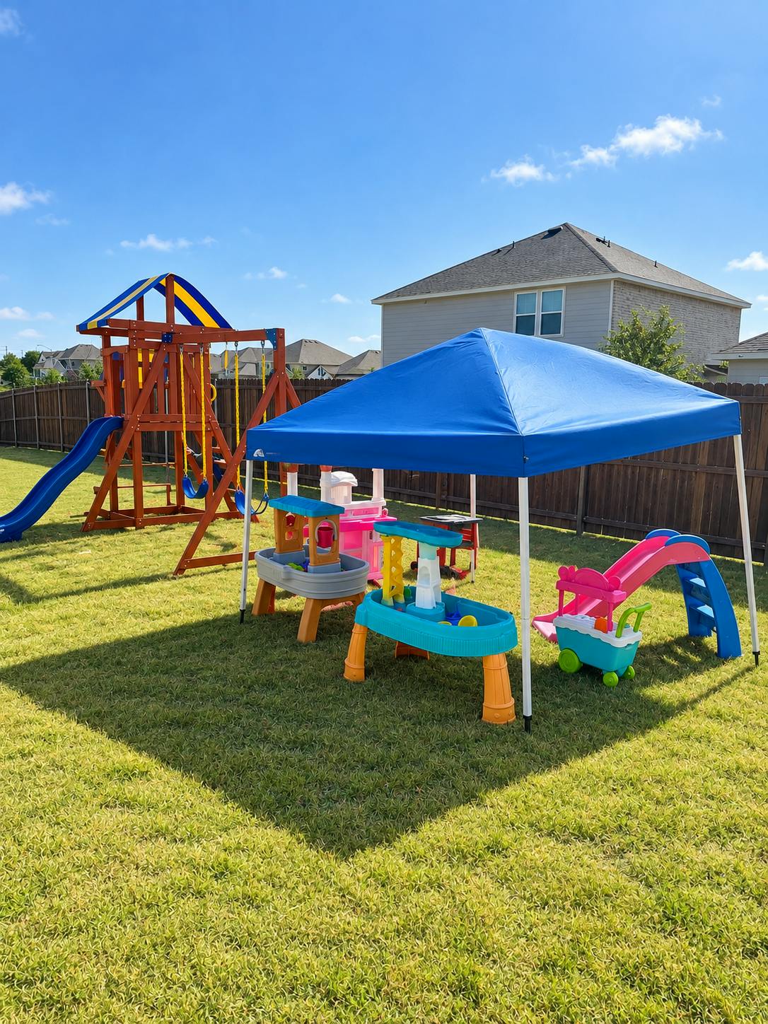 Play equipment and a blue canopy set up on a backyard lawn