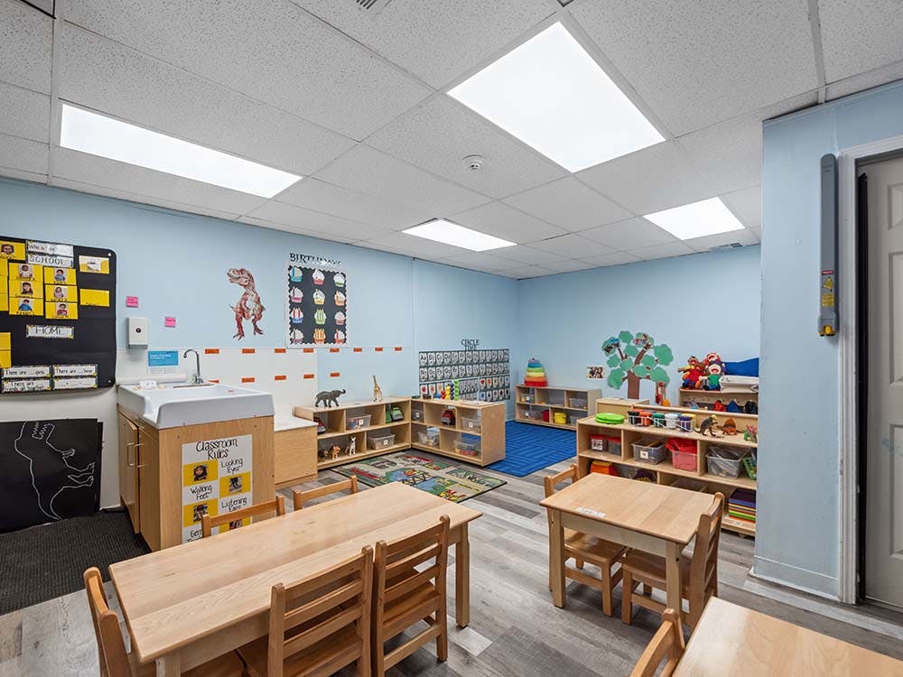 Classroom with small tables, chairs, shelves, and a sink