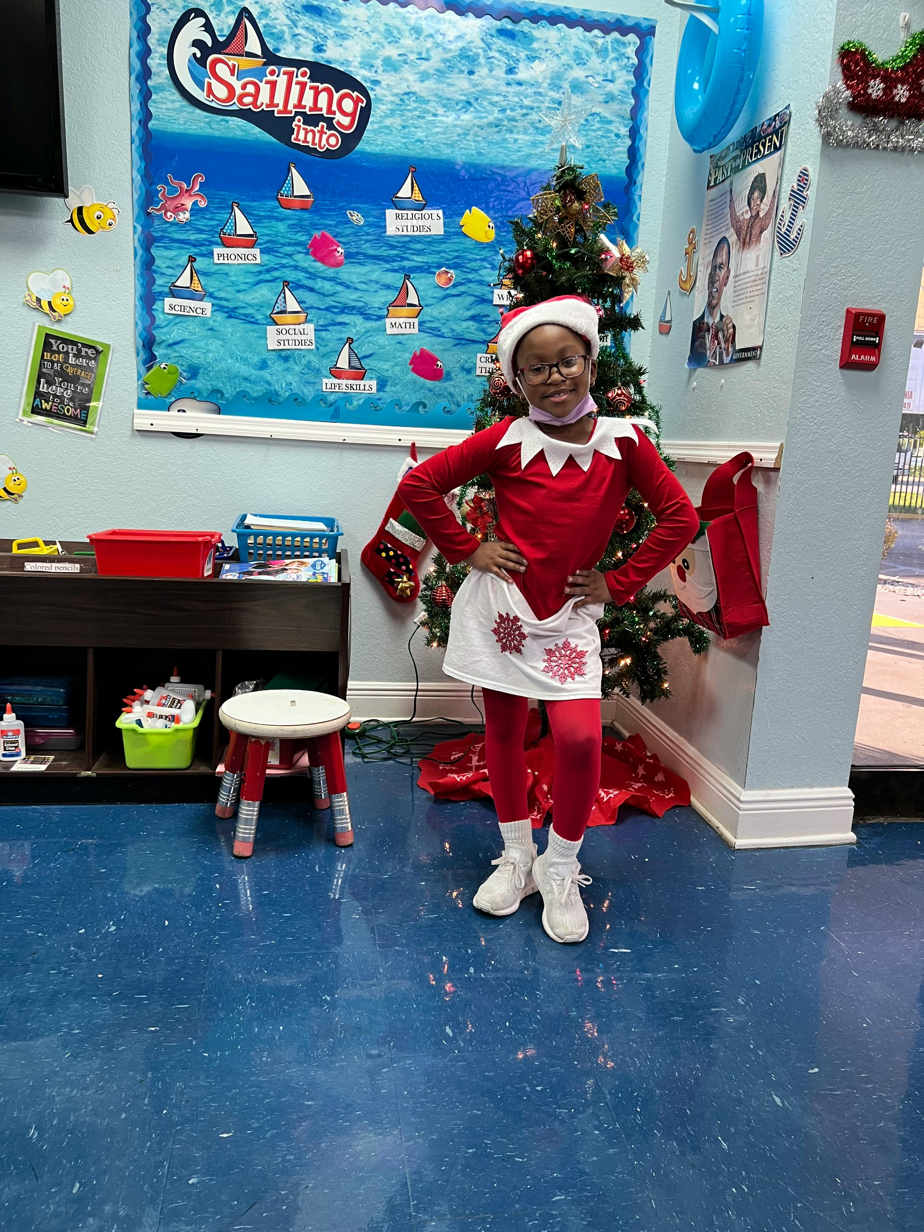 Child in an elf costume standing in front of a Christmas tree