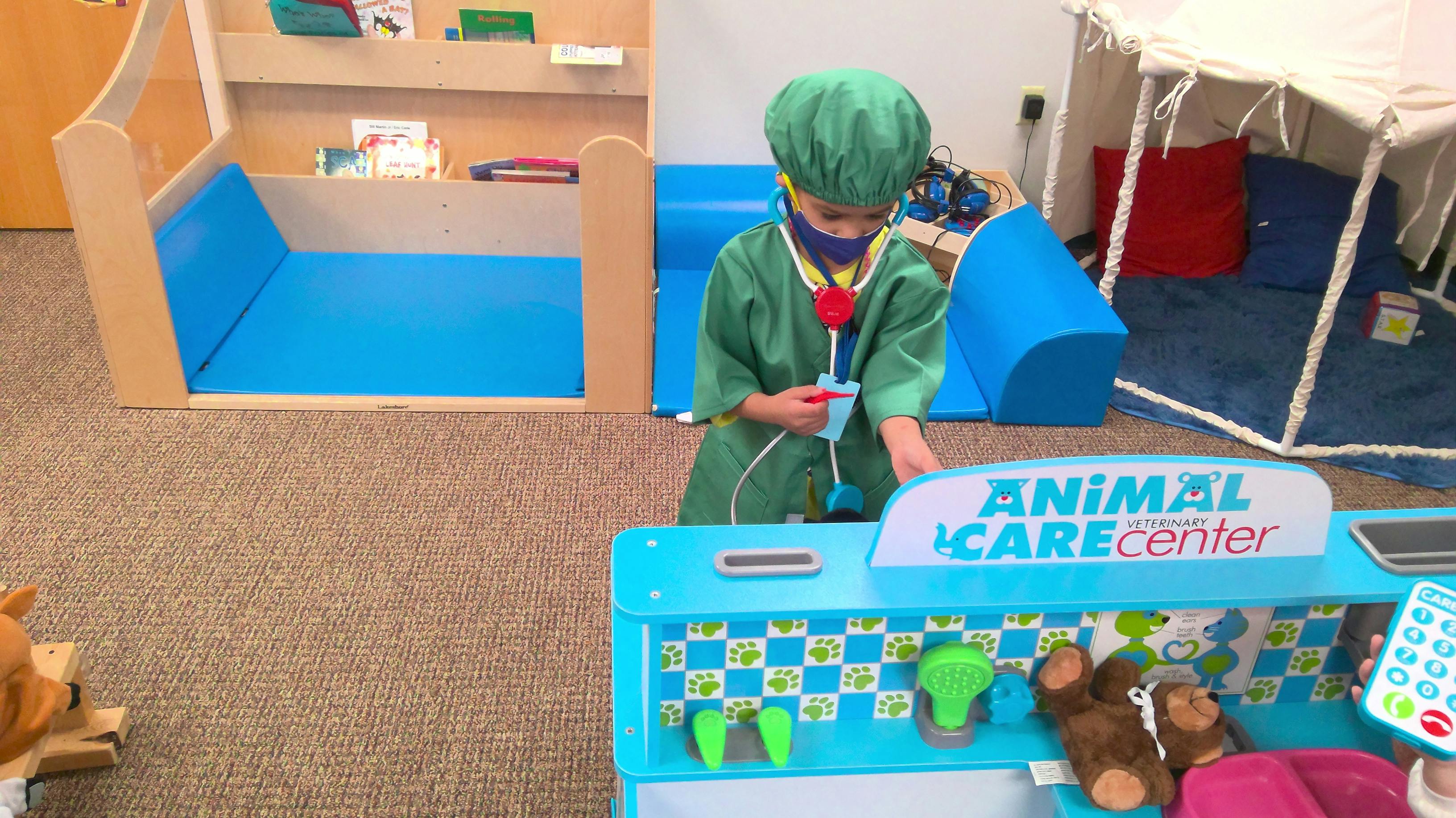 Child in green scrubs and surgical cap playing at an animal care center