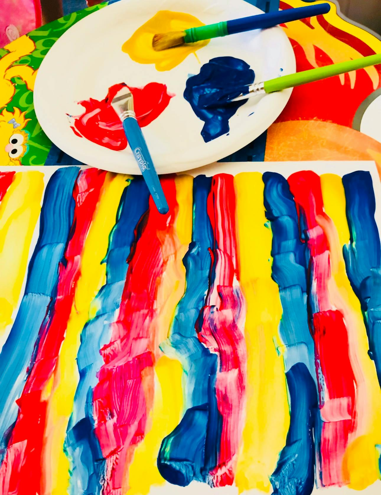 Paint palette with red, yellow, and blue paint, next to a painted paper