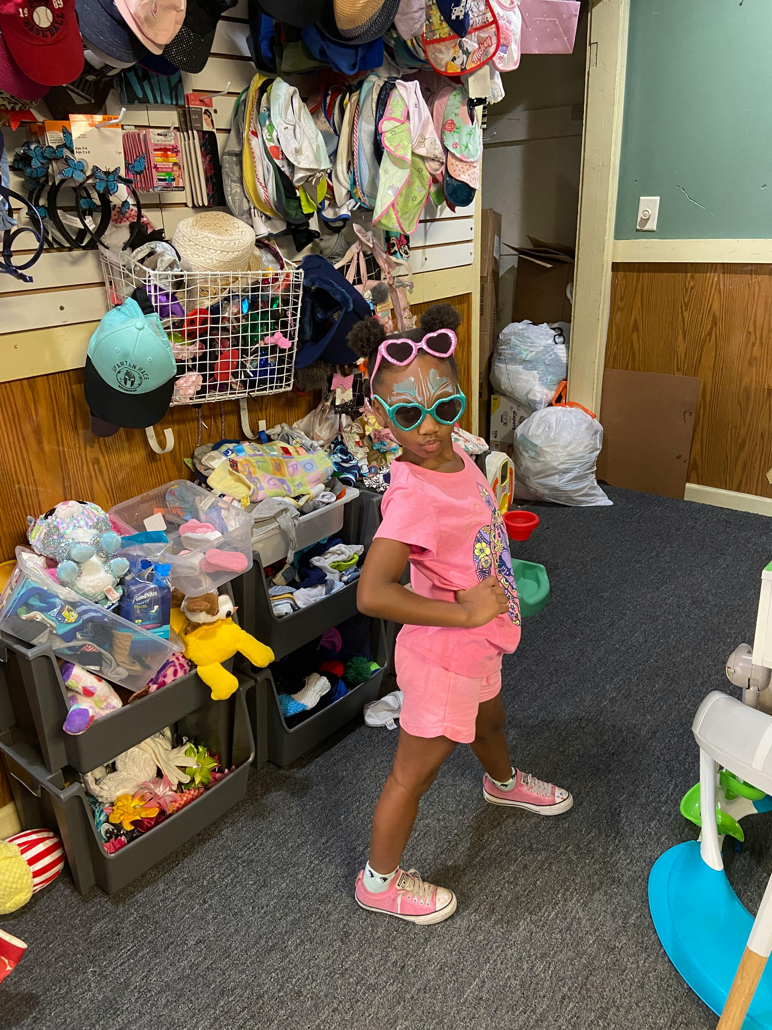 Child in pink outfit and heart-shaped sunglasses posing indoors