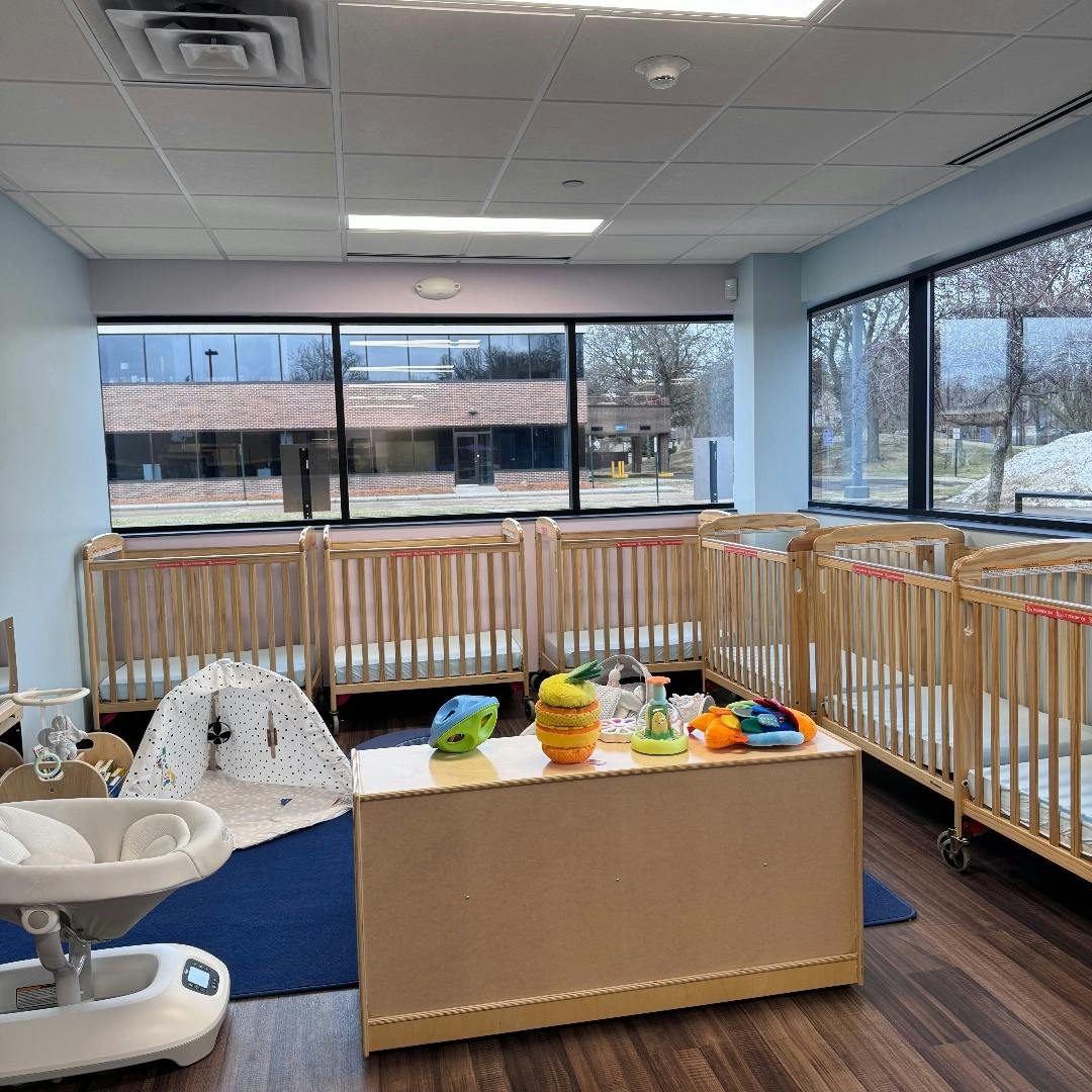 multiple cribs with mattresses next to large windows overlooking a parking lot