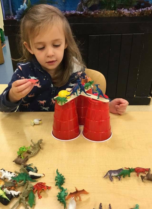 Child playing with toy dinosaurs and red cups