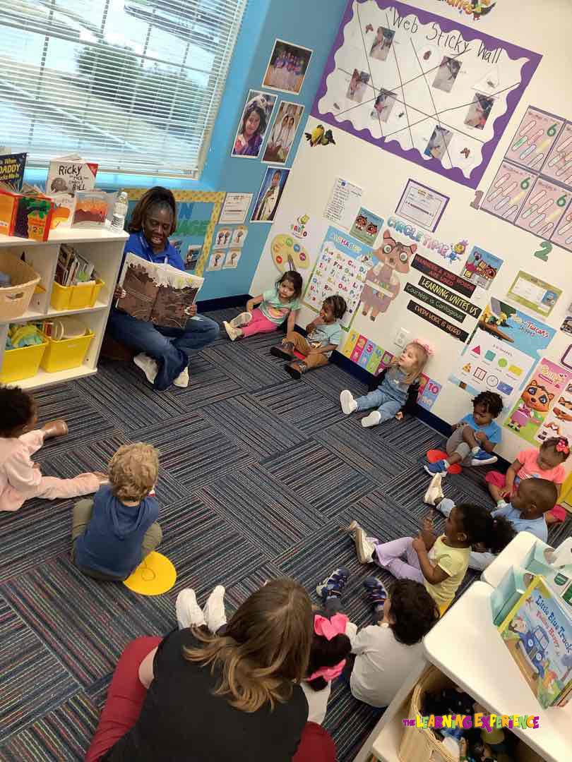 person reading book to group of children sitting on floor in classroom
