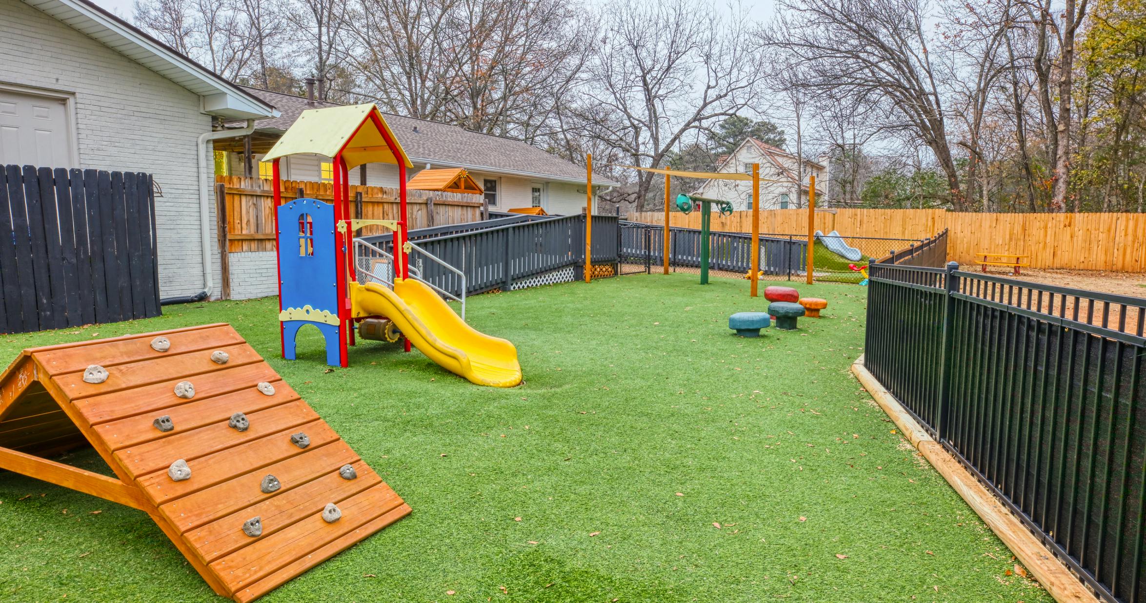 Playground with climbing structure, slide, monkey bars, and soft seating on green turf