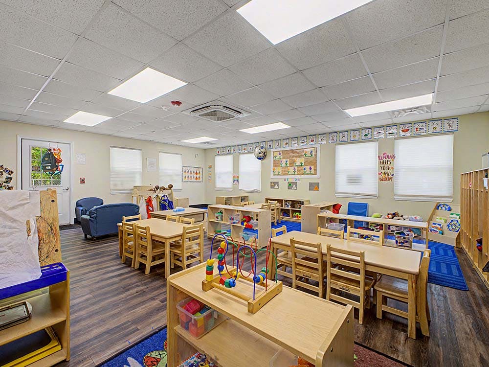 Classroom with small wooden tables and chairs, shelves, and a sofa