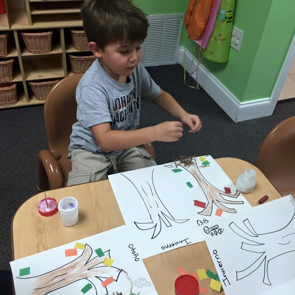 Child sitting at a table doing a craft with paper trees and colorful squares