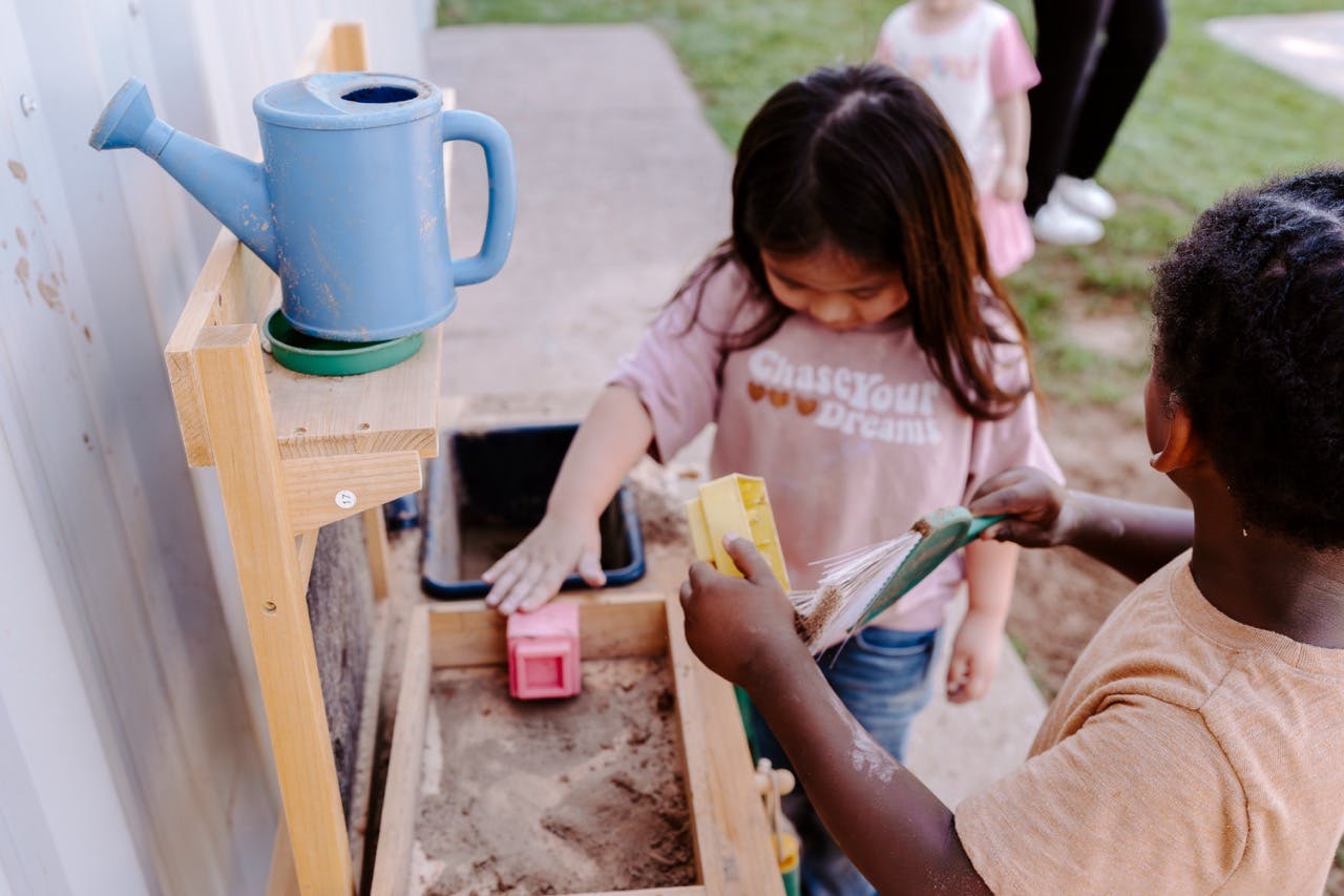 Two children playing with sand and toys at a water table