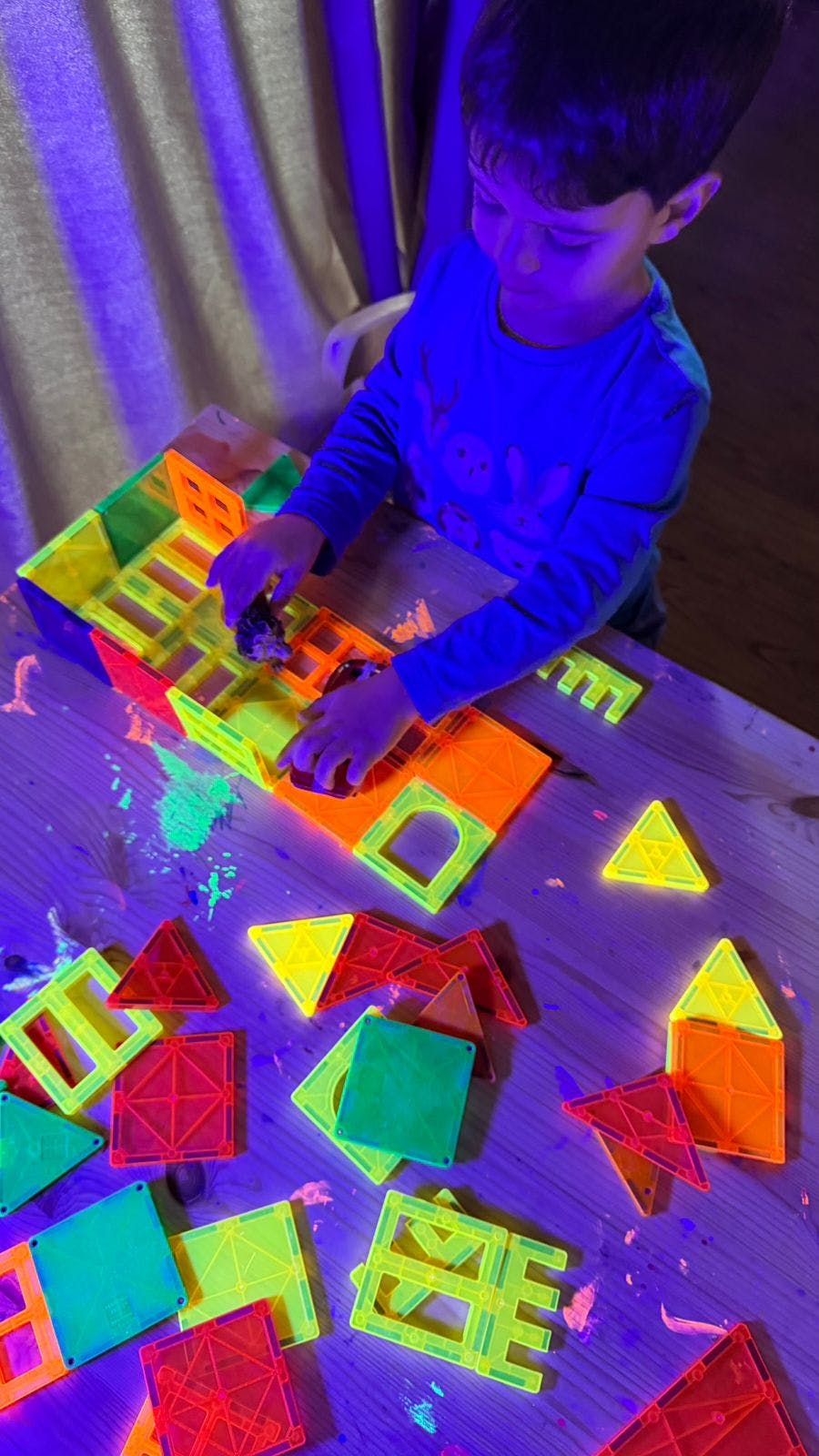 Child playing with fluorescent magnetic tiles under blue light