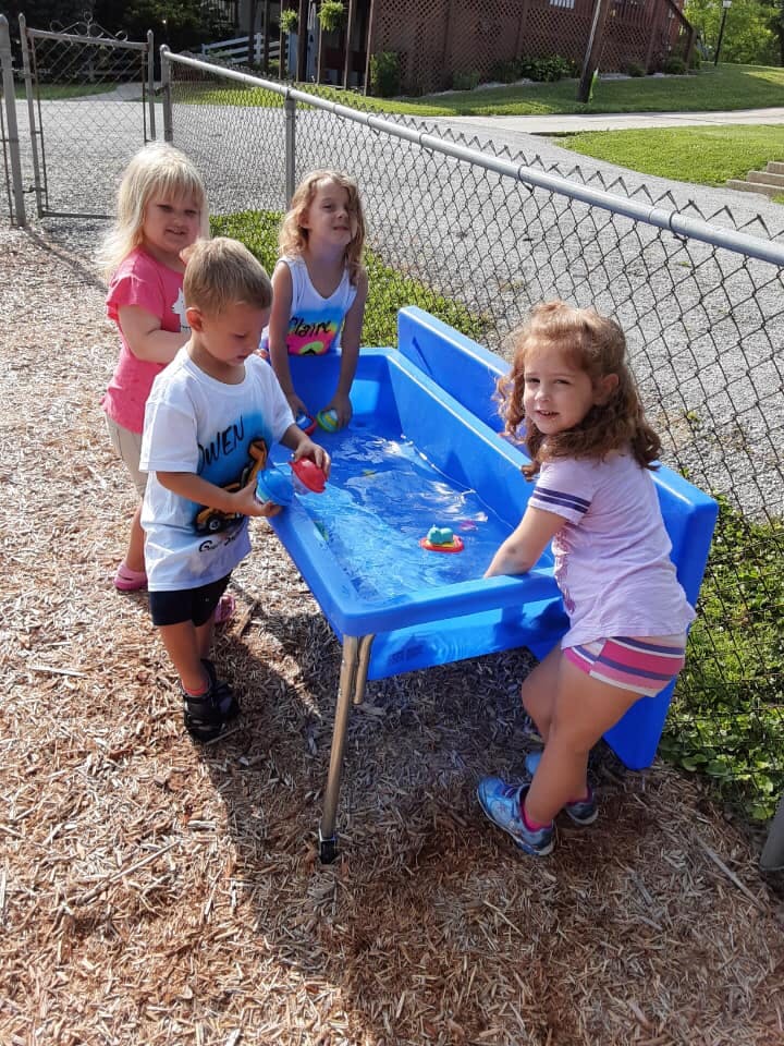Three children playing with a water table outdoors