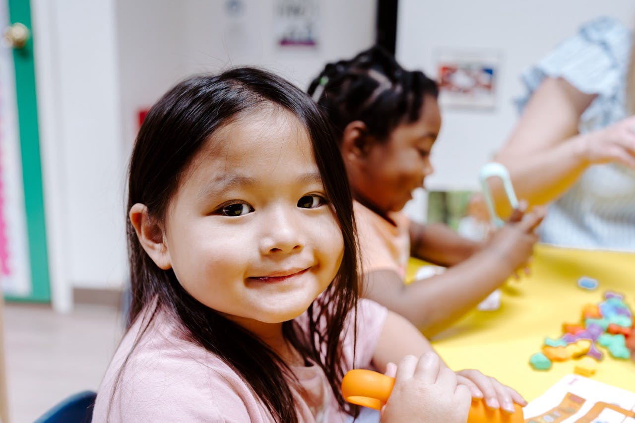 Child smiling at camera while playing with colorful objects at a table