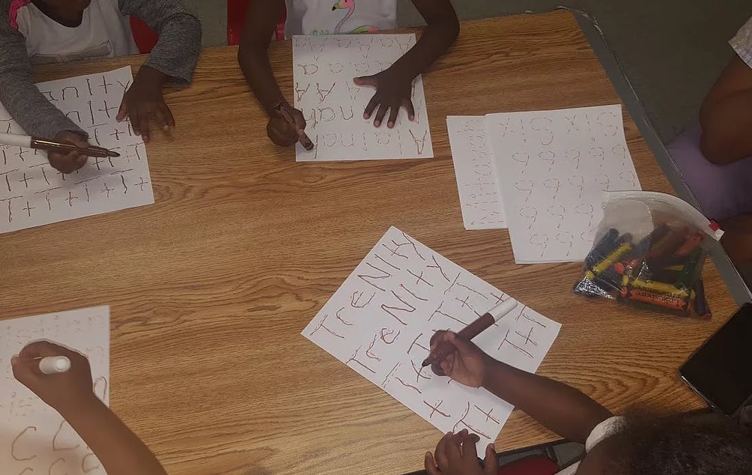 Children writing on paper at a table
