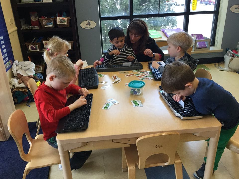 Adult and children at a table with keyboards in a classroom