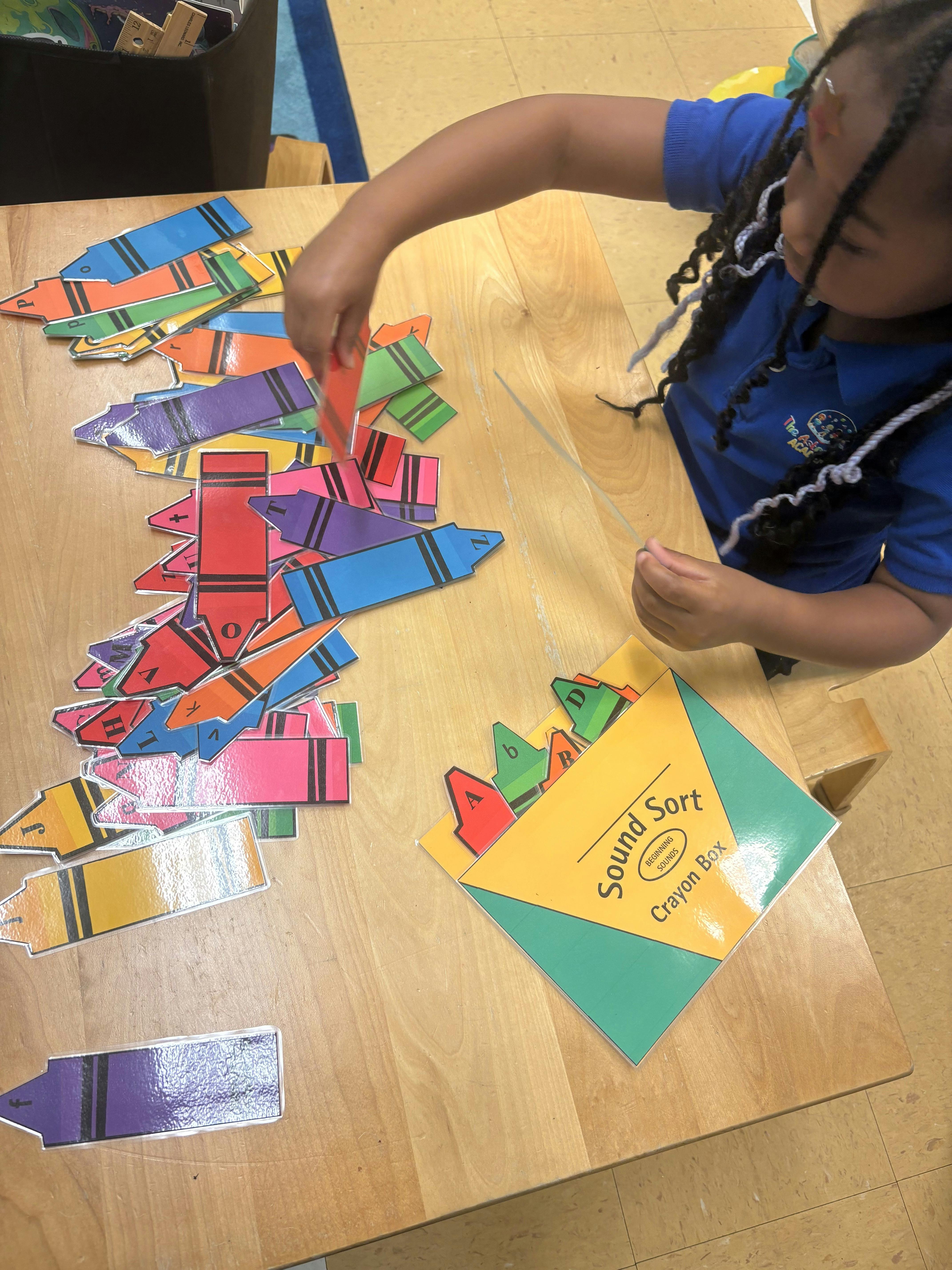 Child sorting colorful crayon cutouts into a box labeled "Sound Sort"