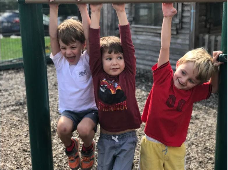 Three children hanging from a bar on a playground