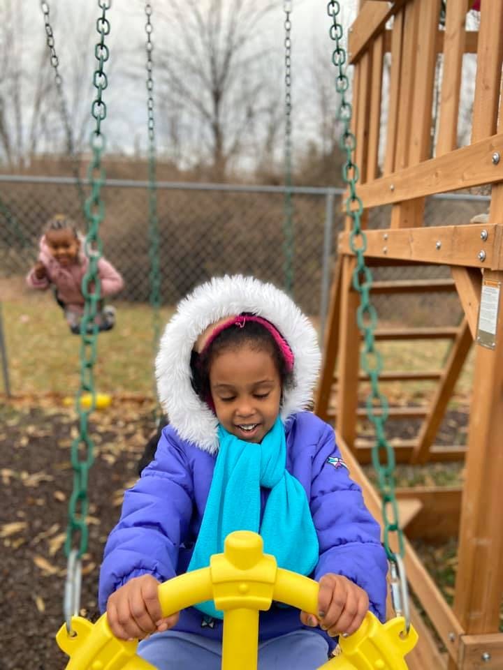Child in a winter coat on a swing, another child in background