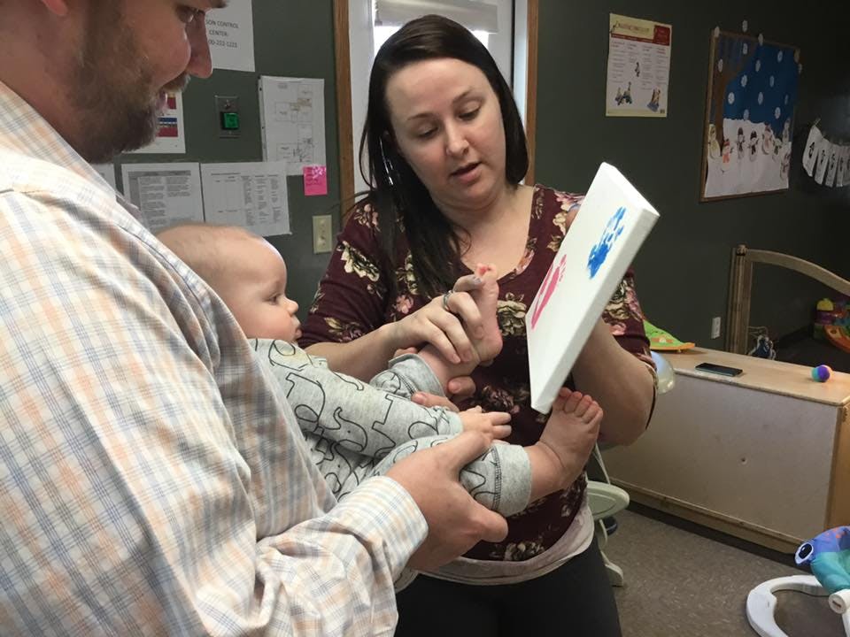 Person holding a child while another person makes a footprint on a canvas