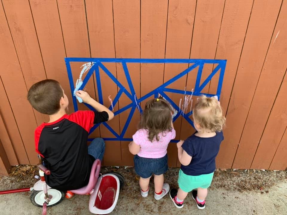 Three children painting on a fence with blue tape