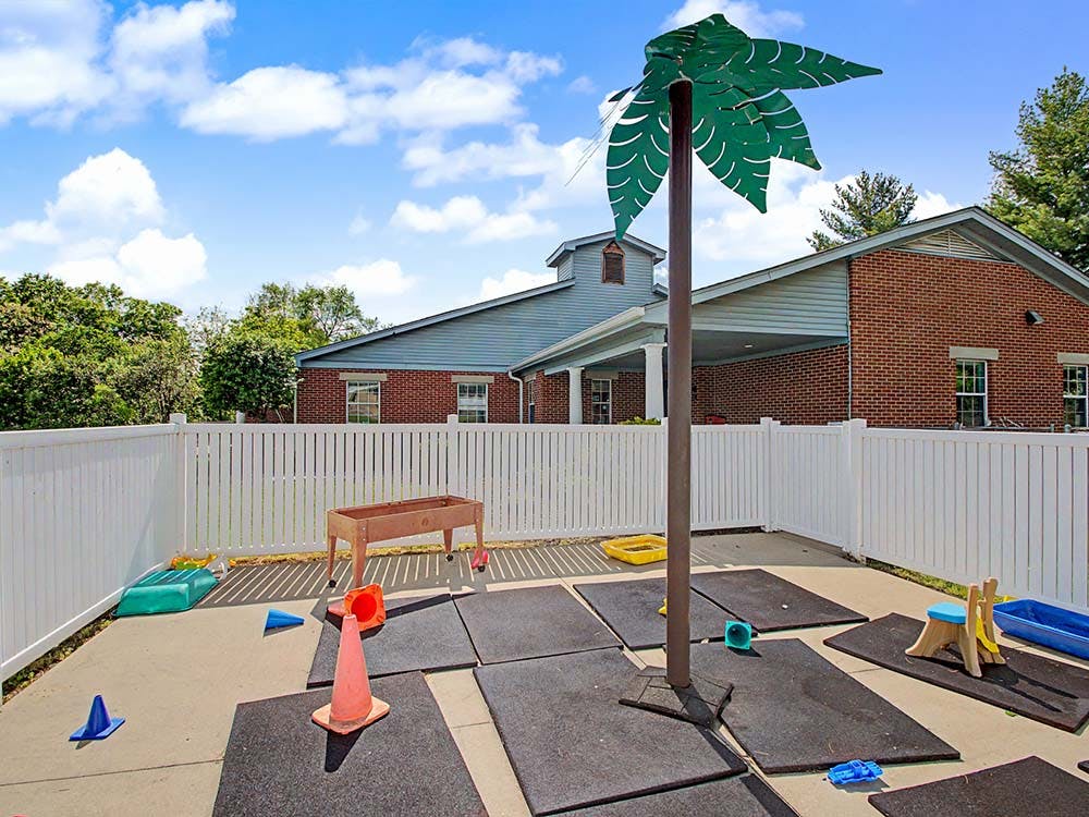 Outdoor play area with rubber mats, toys, and a faux palm tree