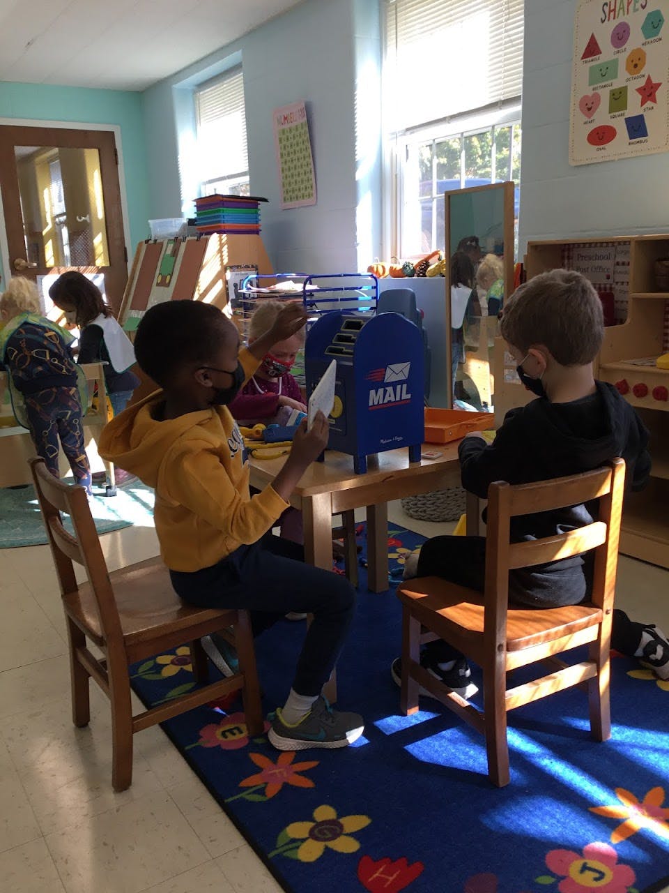 Two children sitting at a table with a toy mailbox in a classroom