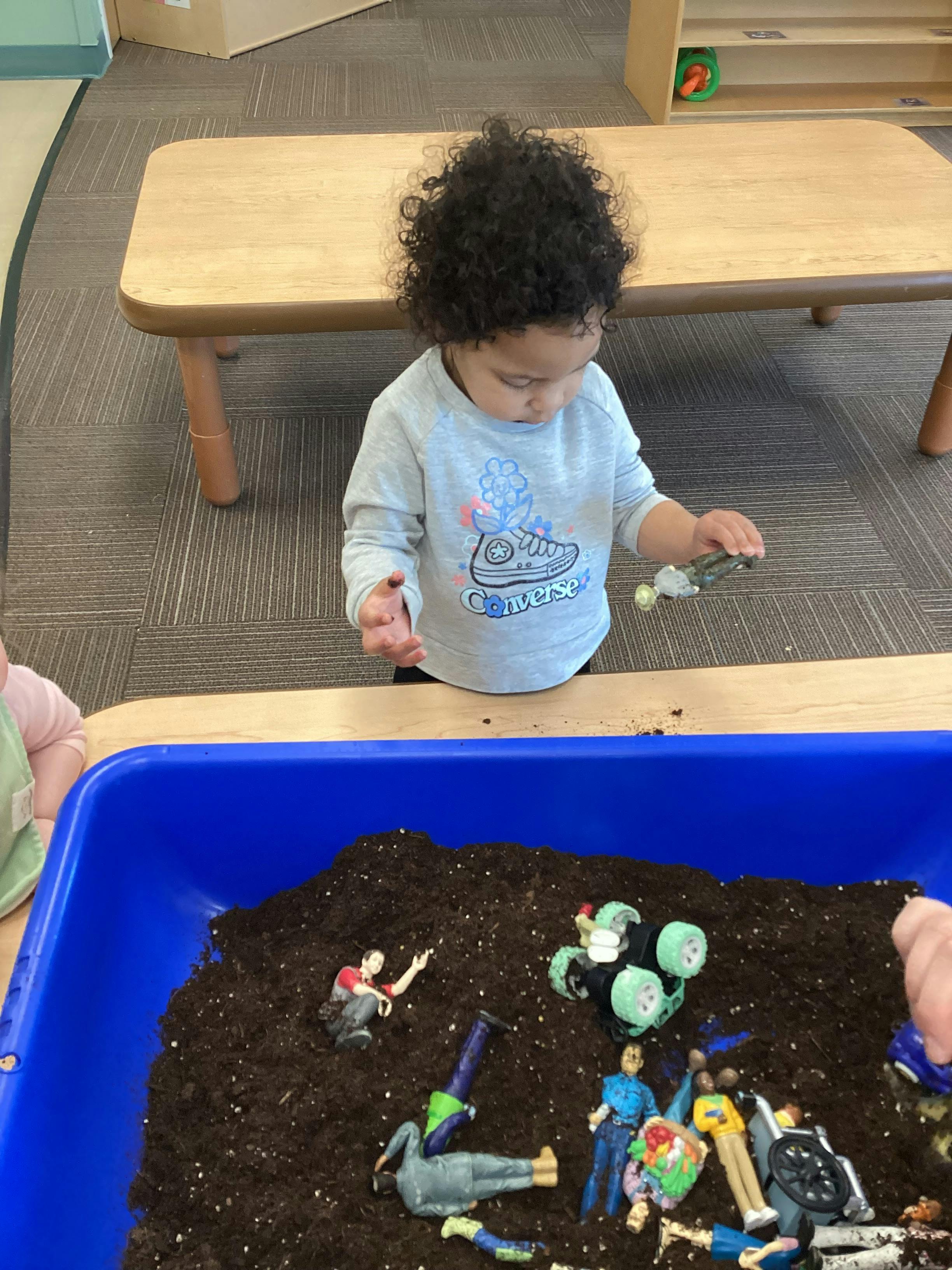 Child playing with a toy in a dirt sensory bin