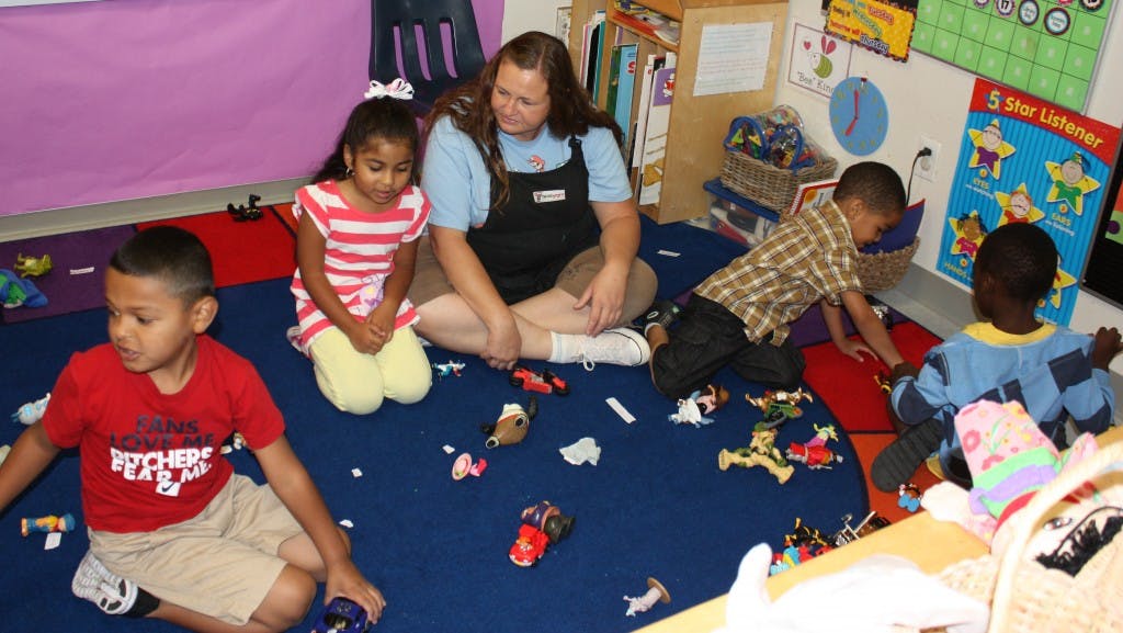 Adult and children playing with toys on a blue mat in a classroom