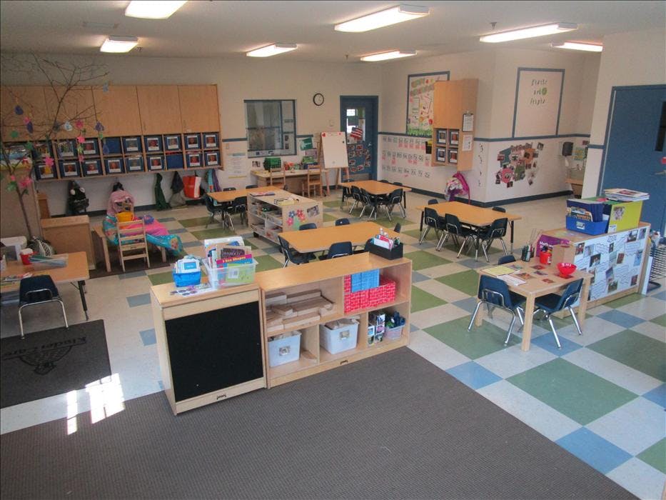An empty classroom with small tables and chairs, shelves, and a checkered floor