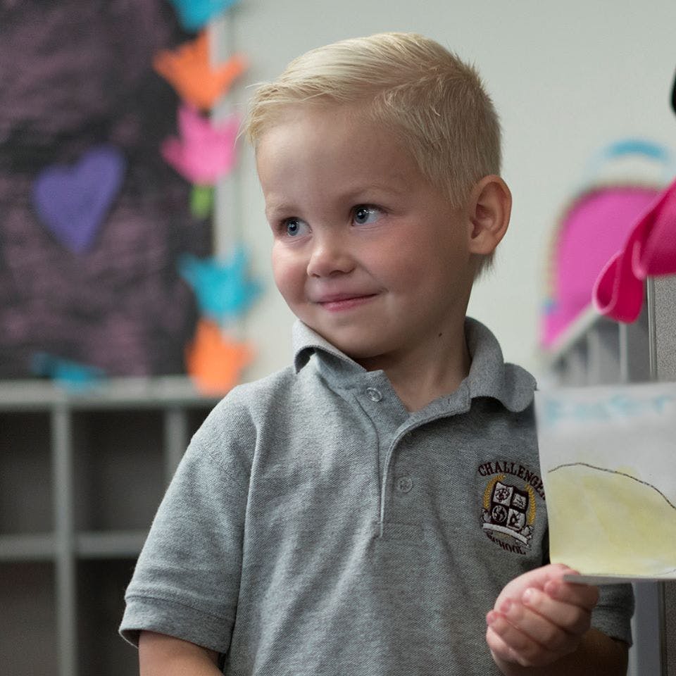 Child in a gray polo shirt holding a piece of paper