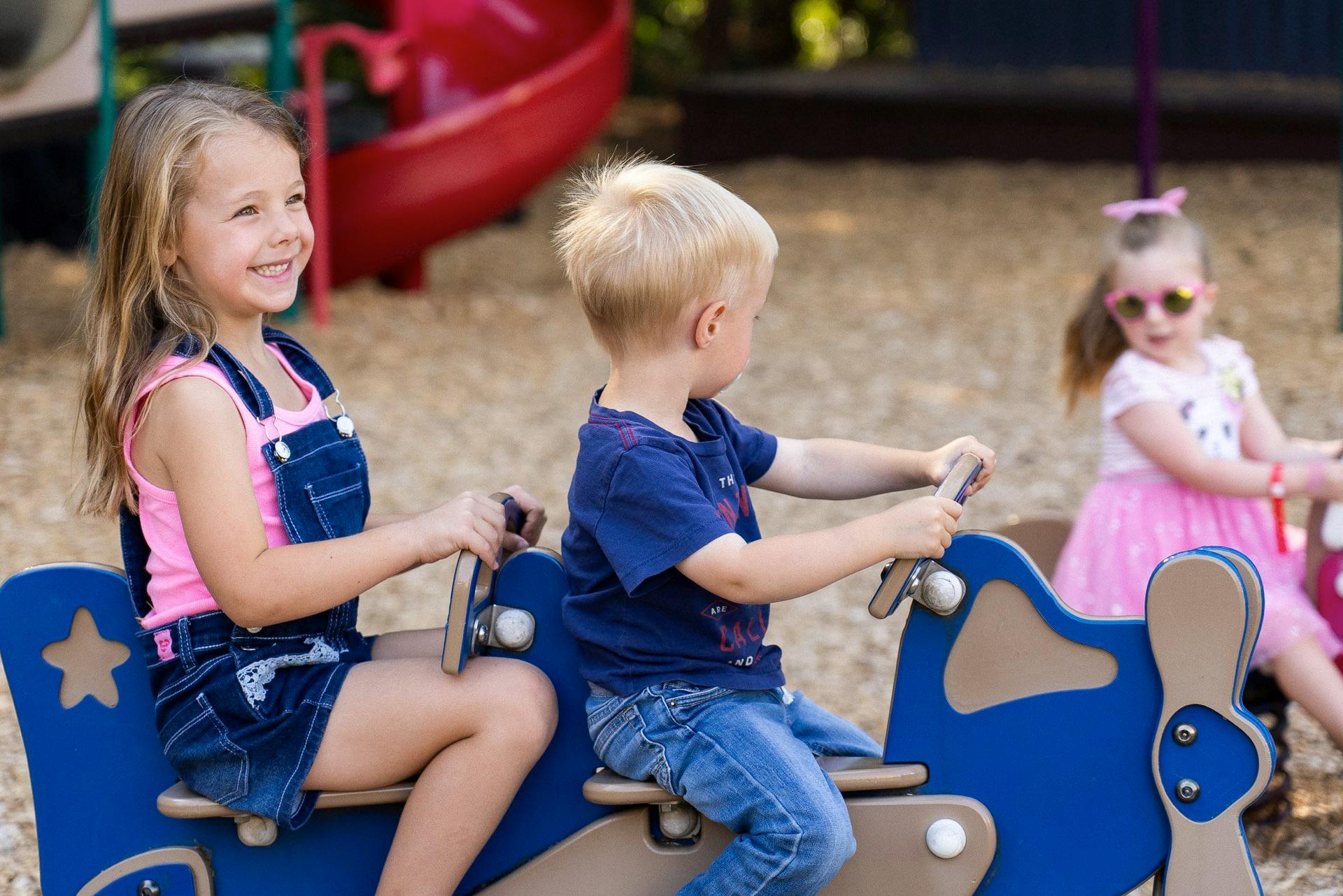 Three children playing on a playground seesaw