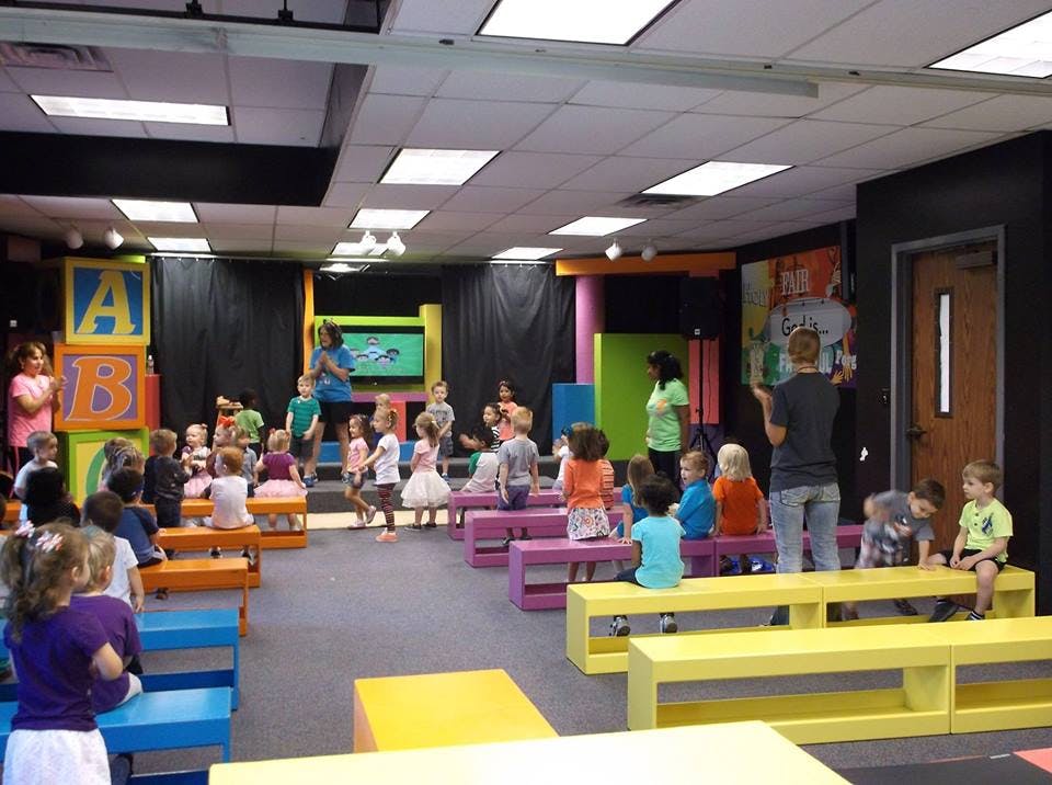 Adults interacting with children in a colorful room with benches