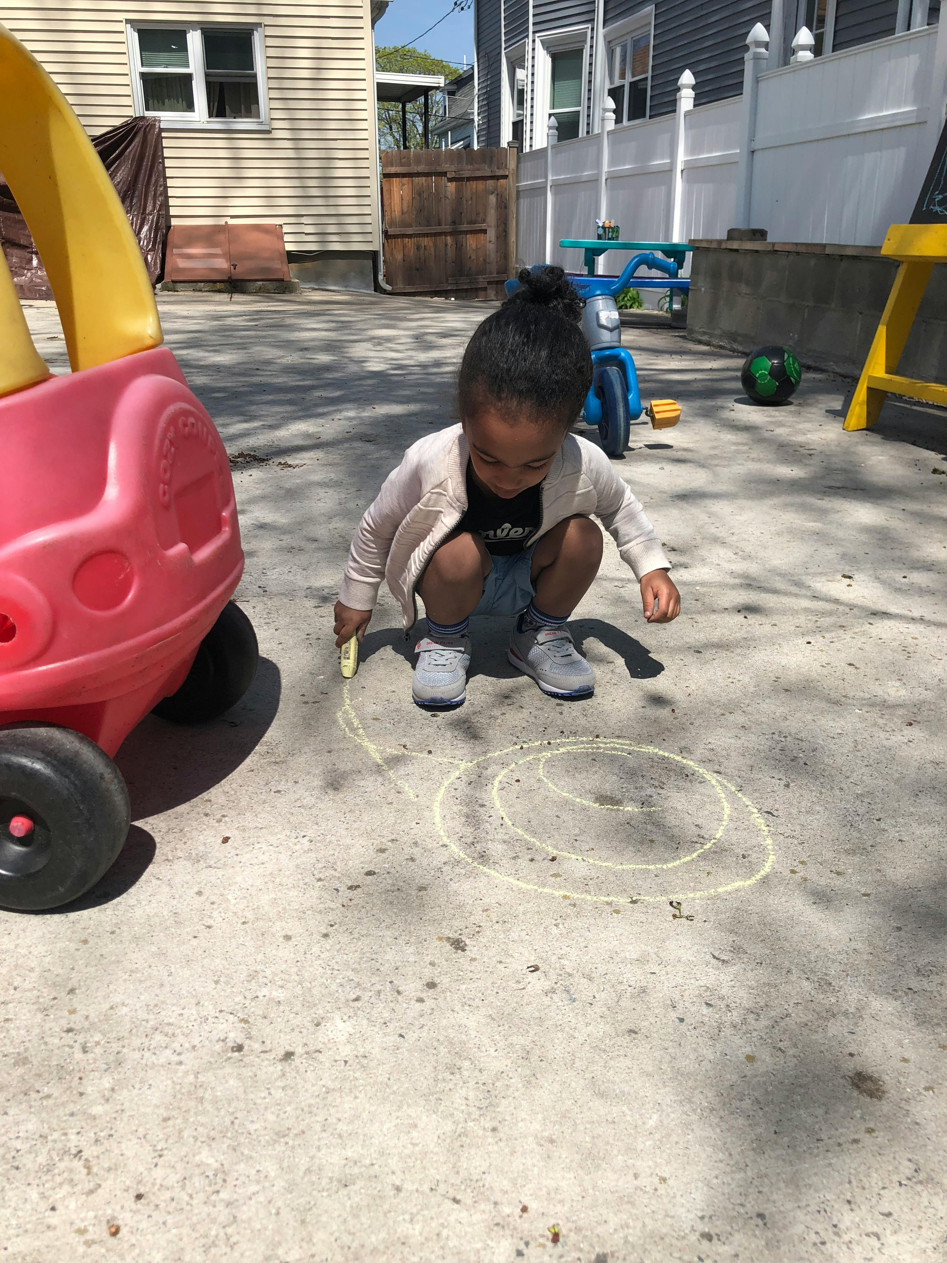 Child crouching and drawing circles with chalk on pavement