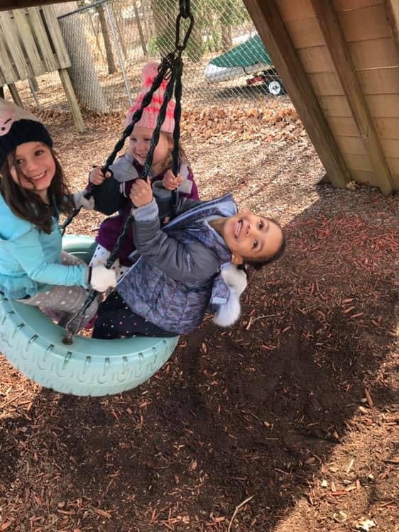 Three children playing on a tire swing and a regular swing