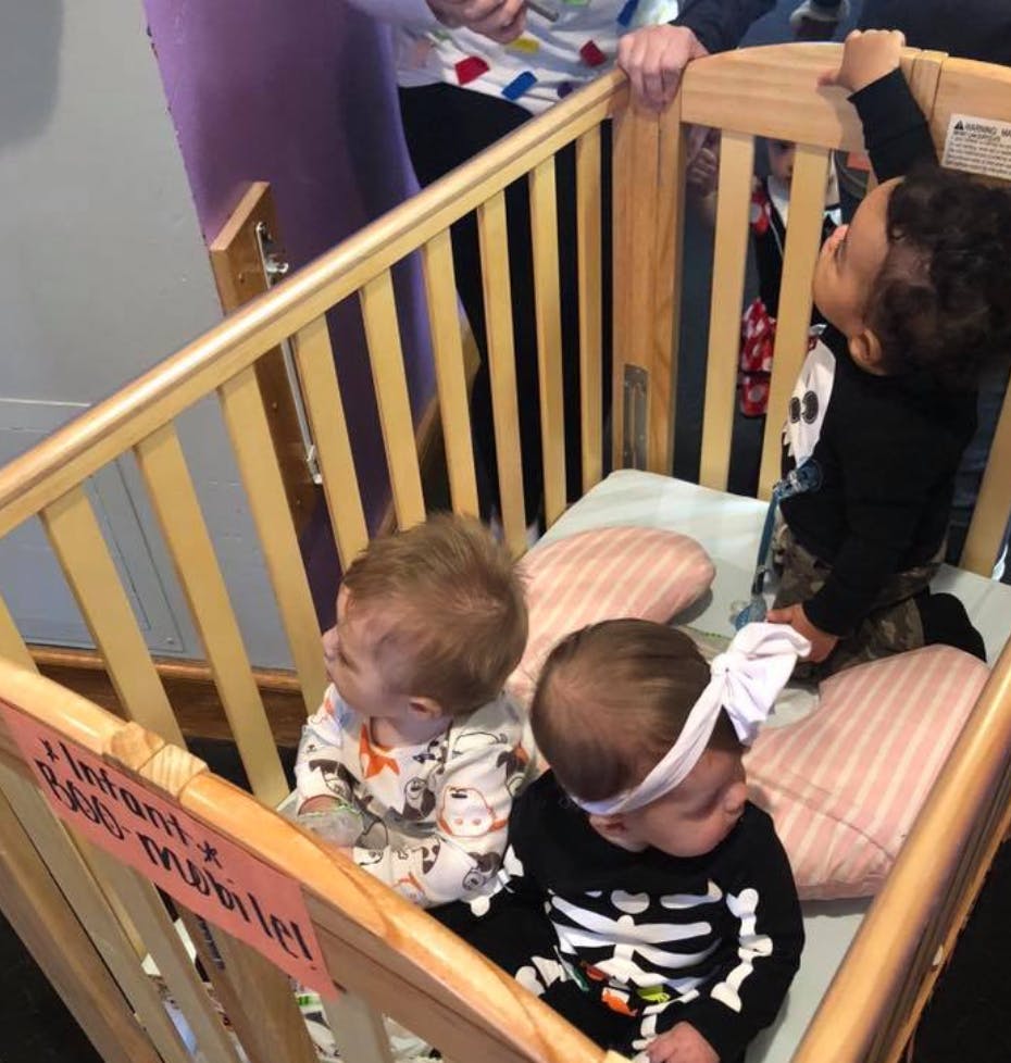 Three children in a crib, one standing and two sitting