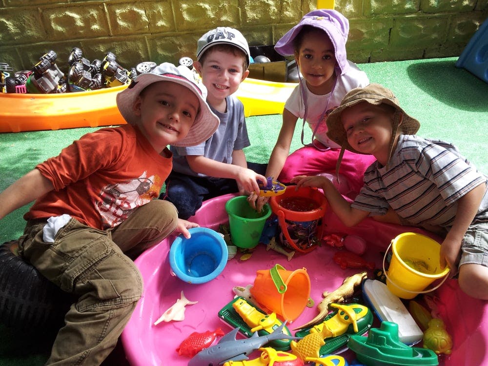 Four children playing with buckets and toys in a pink sandbox