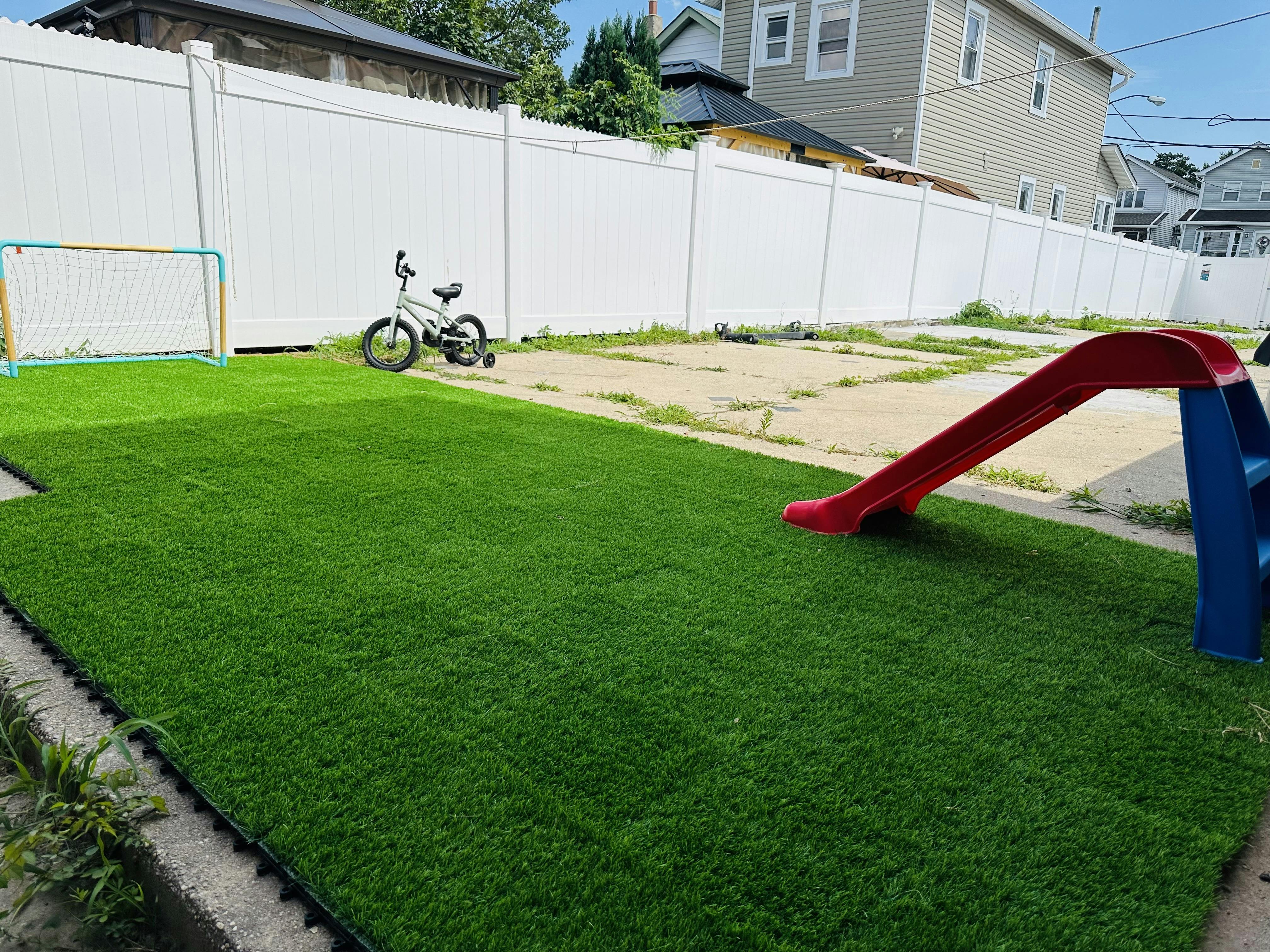 Backyard with artificial turf, a red slide, and a small bicycle