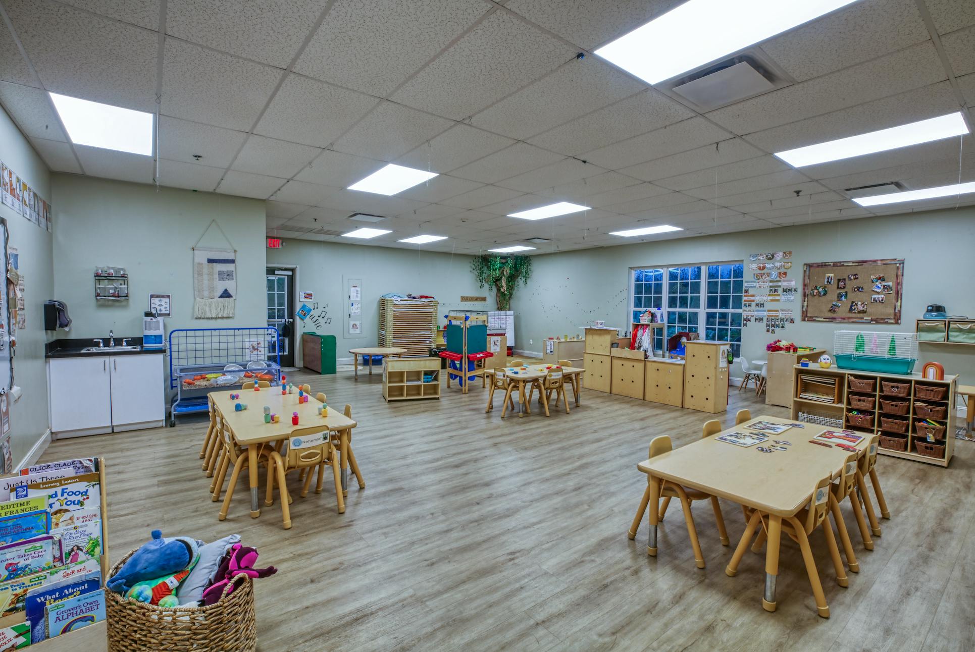 An empty classroom with child-sized tables and chairs, toys, and learning materials