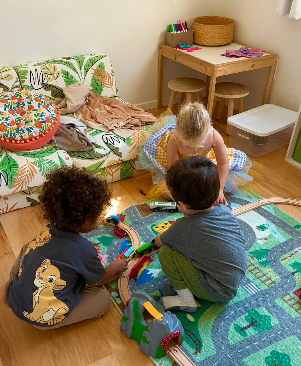 Three children playing with a train set on a rug
