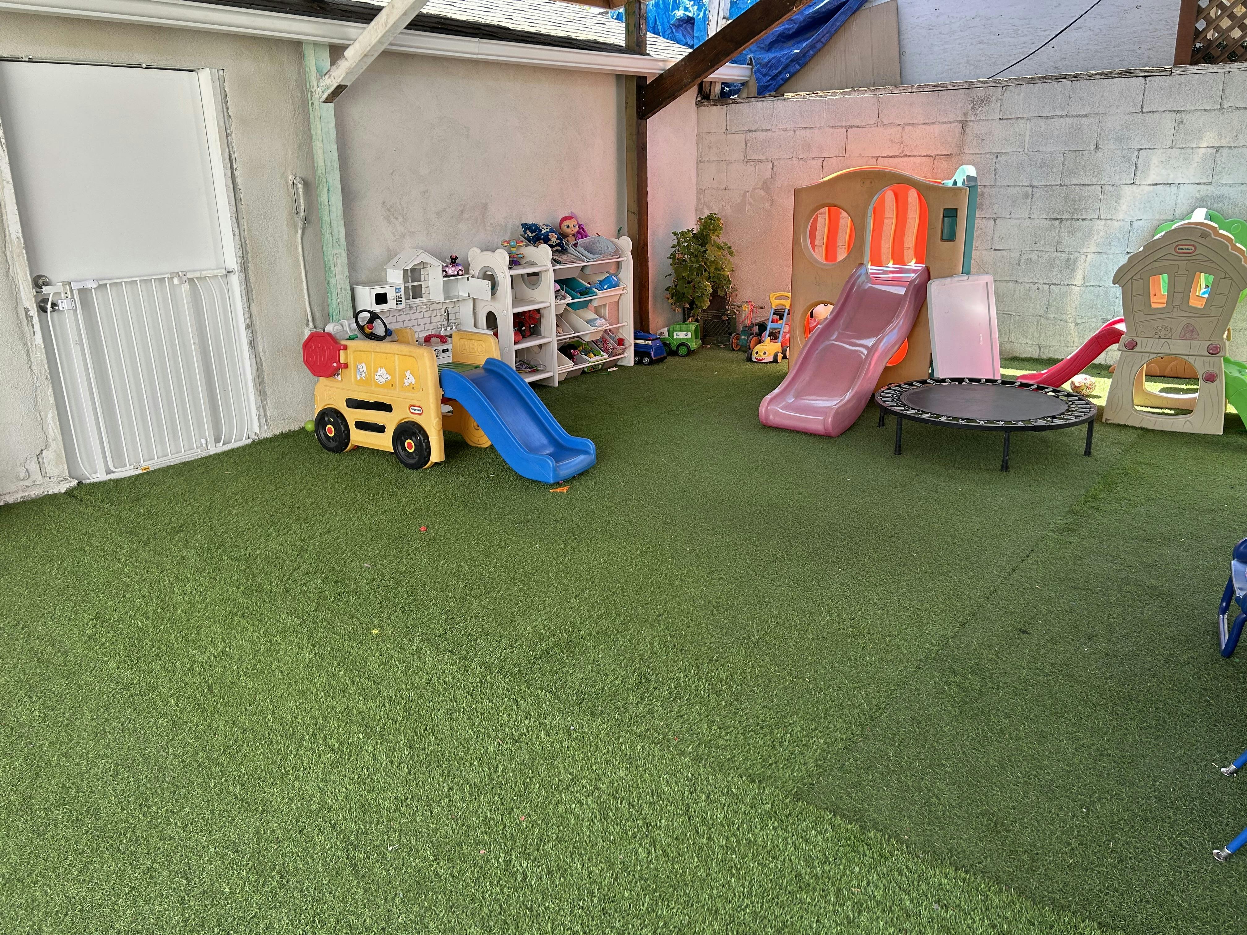 Playground with slides, a trampoline, and a yellow bus toy on green turf