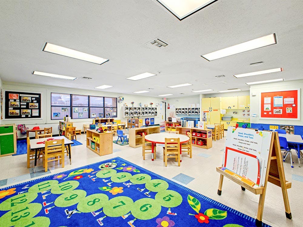 Empty classroom with small tables and chairs, and a blue rug with numbers
