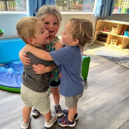 Three children hugging in a classroom