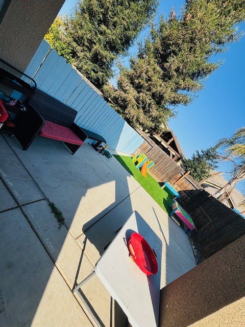 Backyard with concrete patio, blue fence, and artificial turf with toys