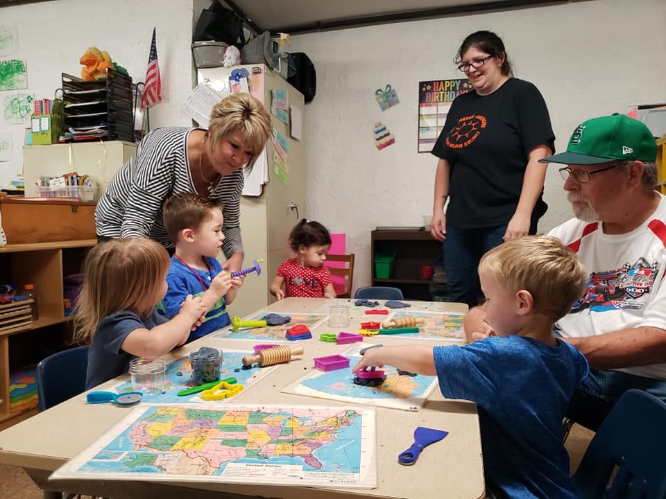 Adults and children at a table with playdough and maps in a classroom