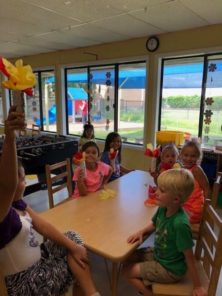 Children sitting at a table in a classroom, some holding crafts
