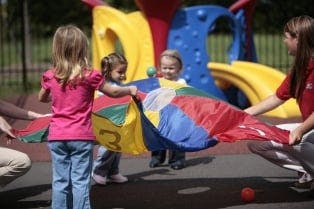 Children and adults playing with a colorful parachute on a playground