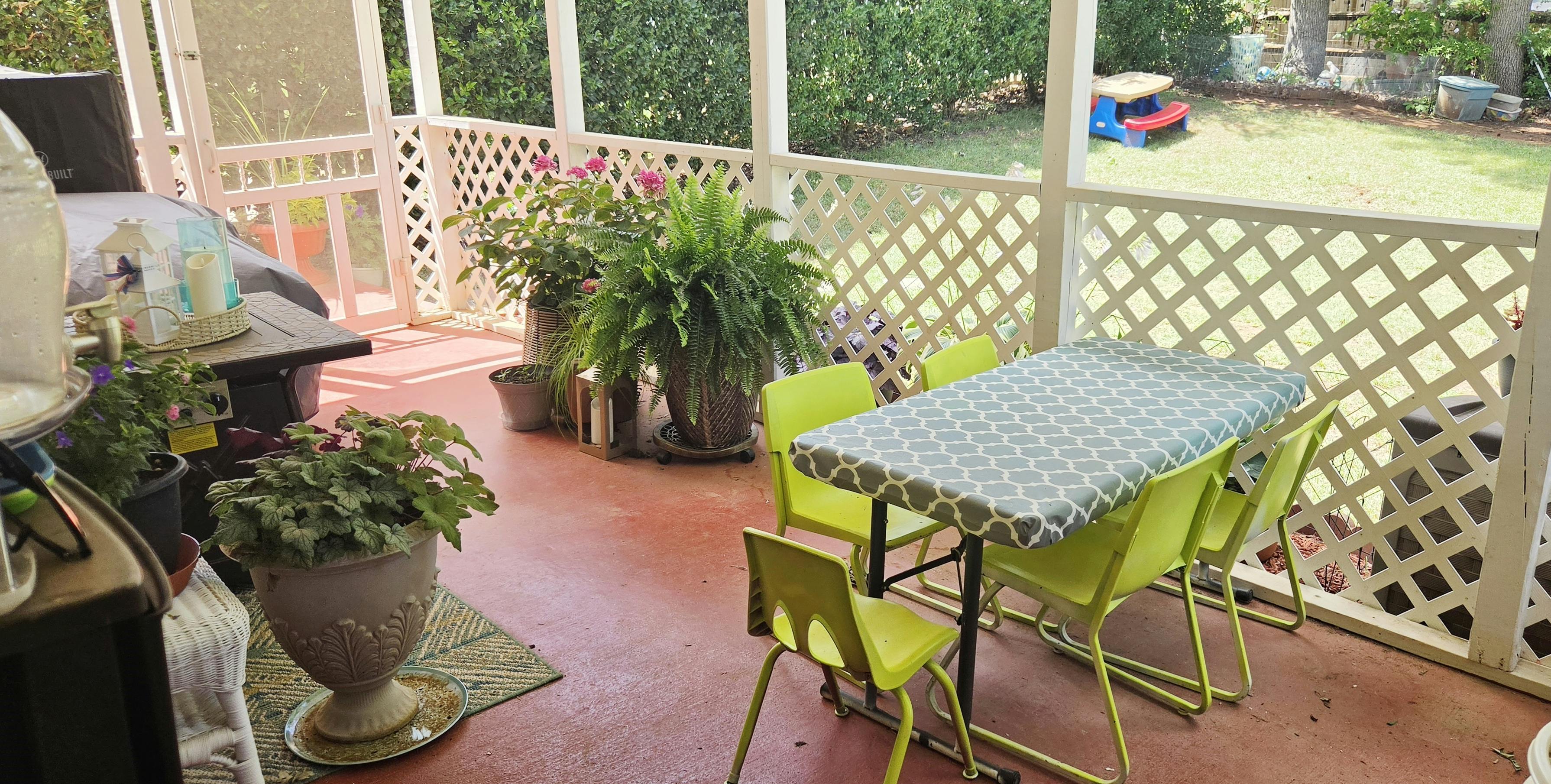 Small table and chairs on a screened porch with potted plants