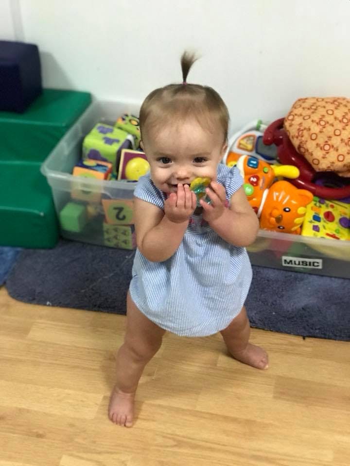 Child standing and holding a toy to their mouth